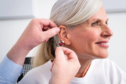 Ältere Frau beim Anpassen eines modernen Hörgeräts durch einen Hörakustiker.